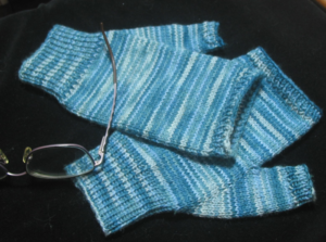 handknit fingerless mitts, variegated stripey ocean blue against a black background with a pair of glasses.